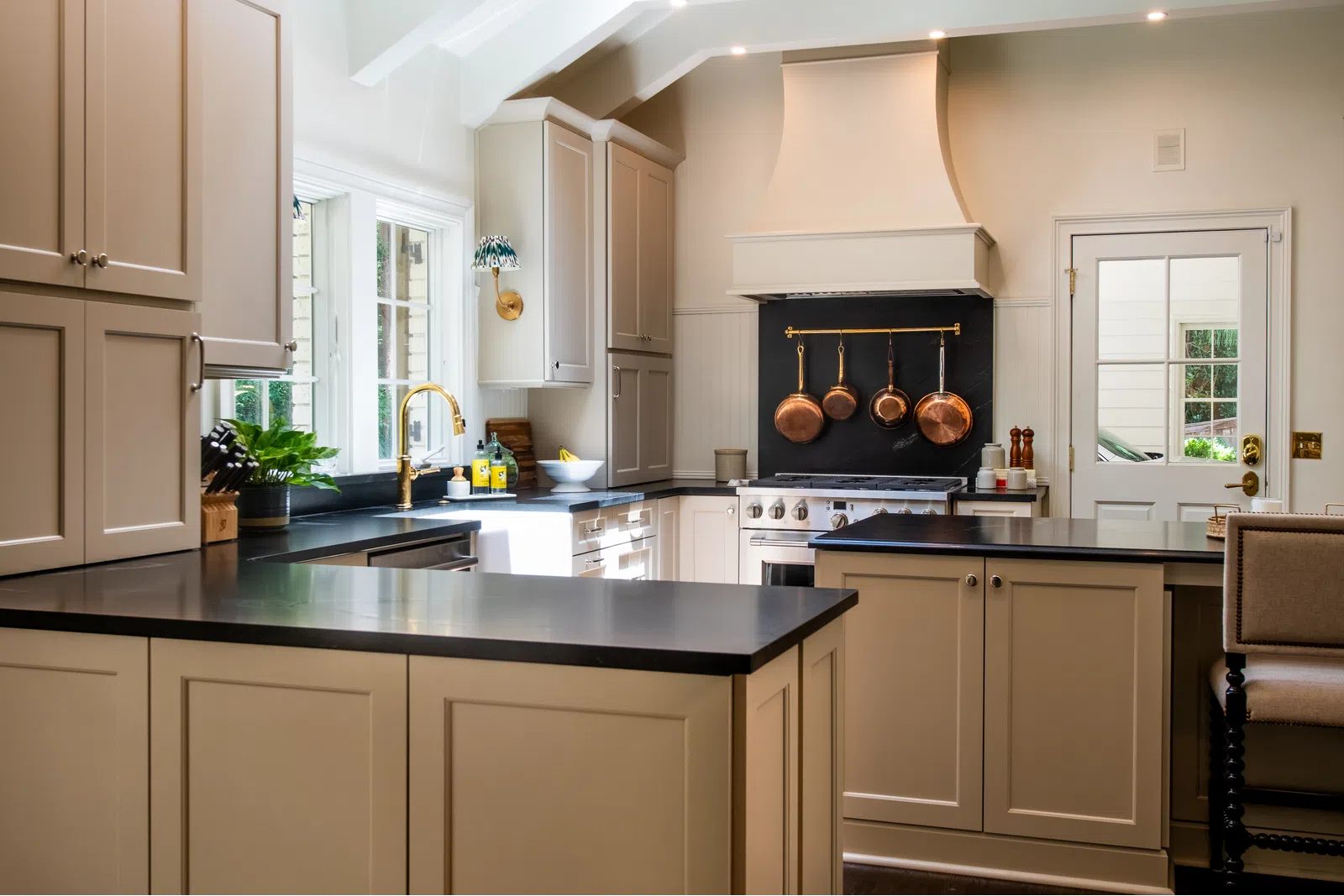Bright modern kitchen with beige cabinets, black countertops, copper pots, and a large window for natural light