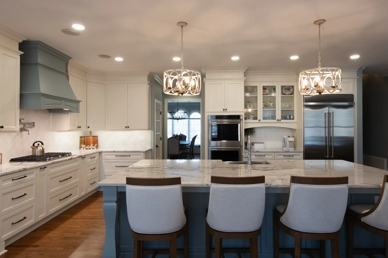 Spacious modern kitchen with white cabinetry, marble island, stainless steel appliances, and wooden floor.