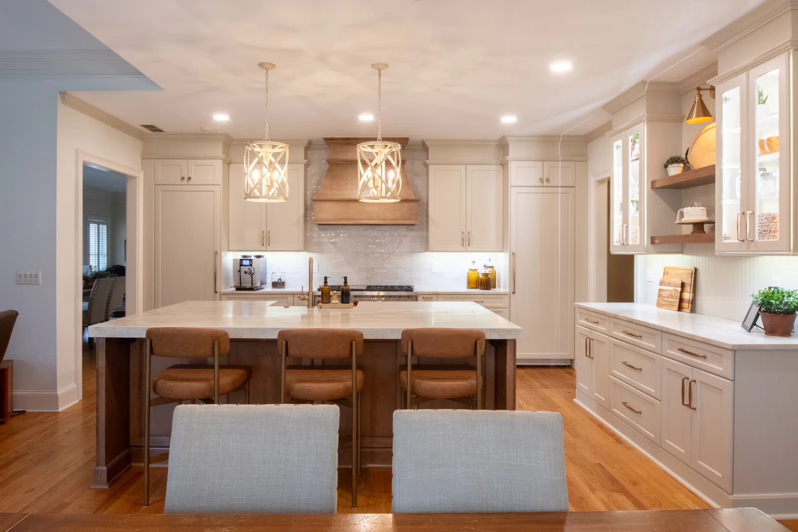 Modern kitchen with white cabinets, wooden island with brown chairs, pendant lights, and hardwood floors.
