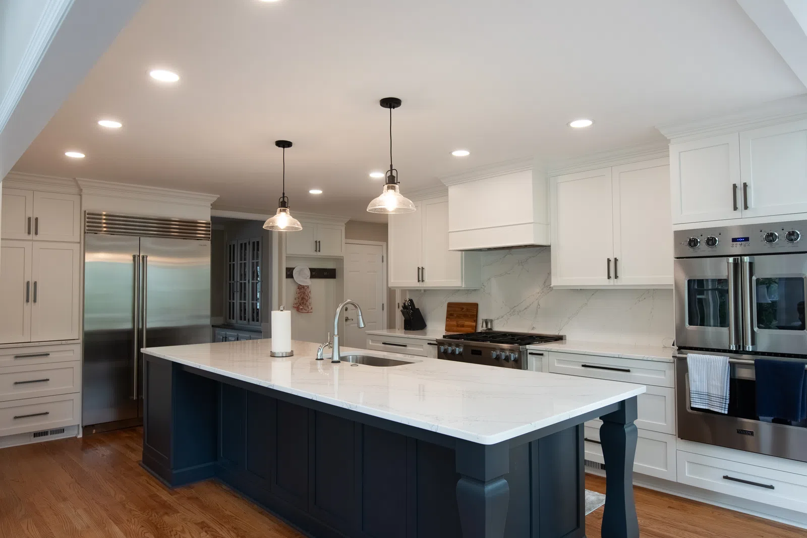 Modern kitchen with white cabinets, marble countertops, large island, stainless steel appliances, and wood flooring