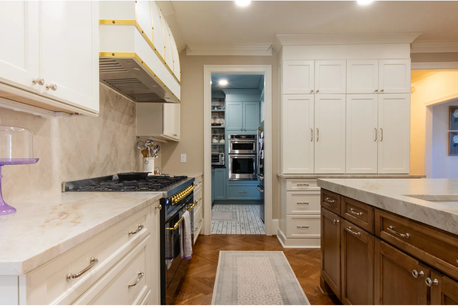 Modern kitchen with white and blue cabinets, marble countertops, wooden island, and built-in oven with gas stove.