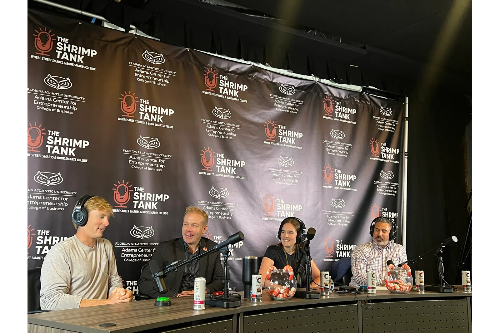 Four people wearing headphones talking into microphones at a Shrimp Tank podcast panel event