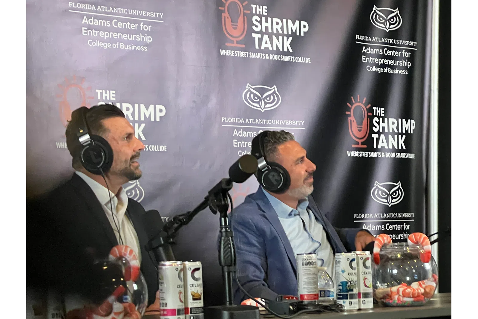 Two men in suits wearing headphones speaking into microphones during The Shrimp Tank podcast at Florida Atlantic University.