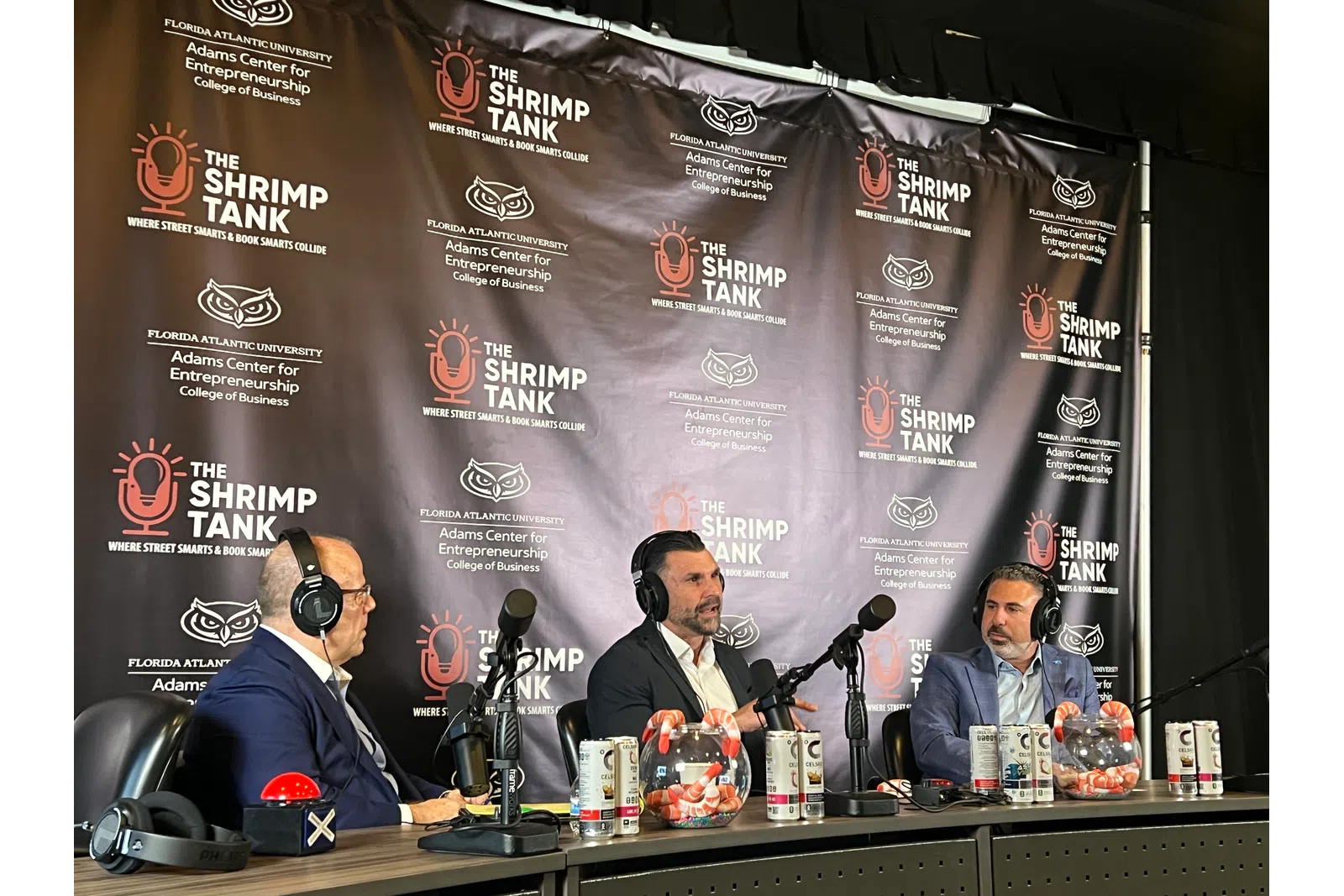 Three men wearing headsets talk into microphones during a Shrimp Tank podcast recording with branded backdrop.