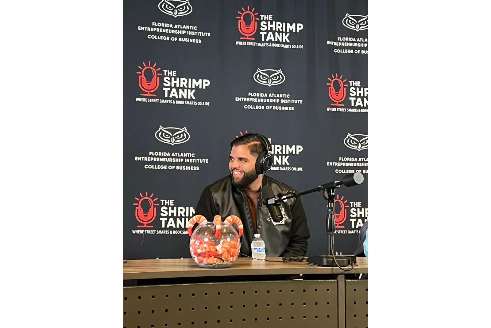 Man wearing headphones speaking on a podcast with shrimp-themed decorations and Shrimp Tank banners behind him.