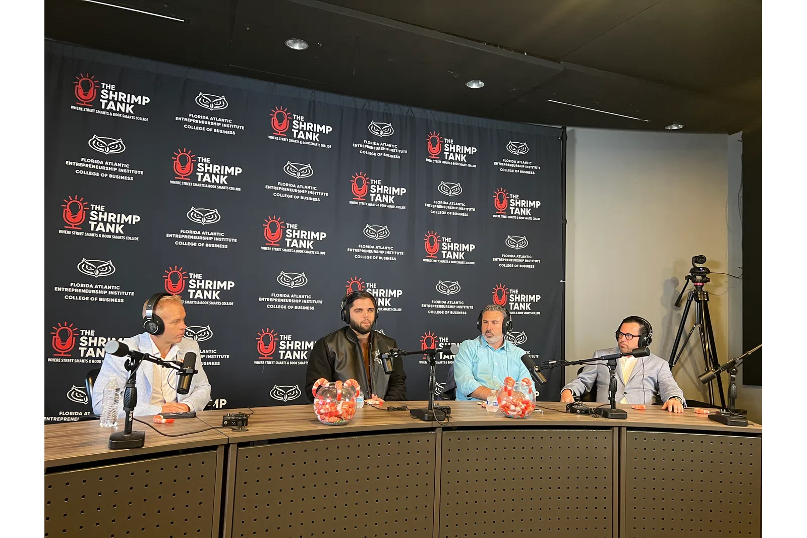 Four men seated at a podcast panel table with microphones and headphones during The Shrimp Tank event at Florida Atlantic University.