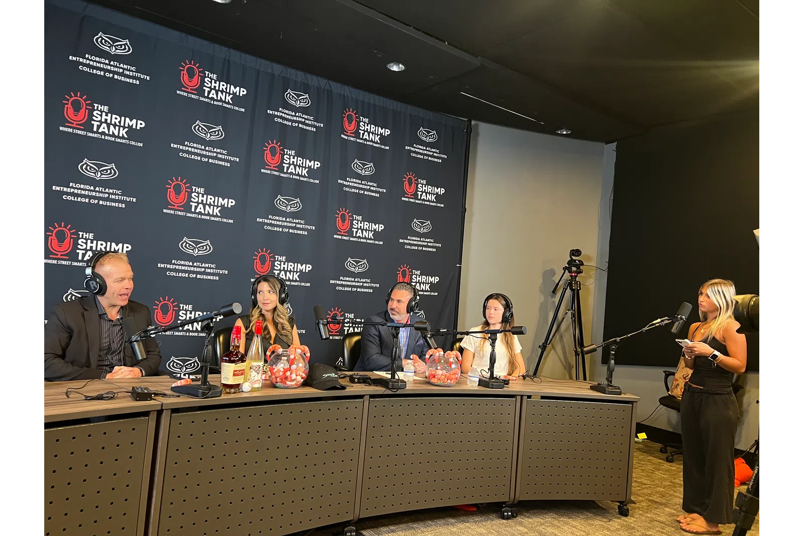 Podcast recording with four hosts at a table, branded backdrop with overlaid text reading The Shrimp Tank and Florida Atlantic Entrepreneurship logos.
