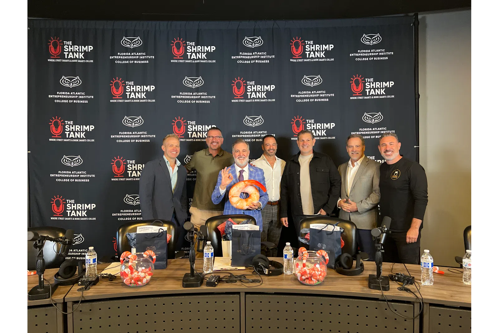 Group of six men standing behind a panel table with microphones and branded backdrop featuring The Shrimp Tank and Florida Atlantic Entrepreneurship logos.