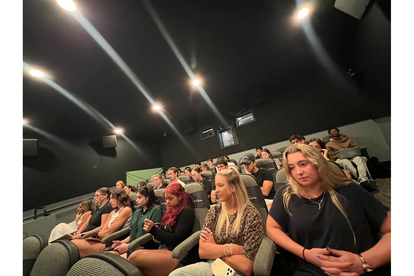 Diverse group of people attentively watching a presentation or film in a dark auditorium with tiered seating.