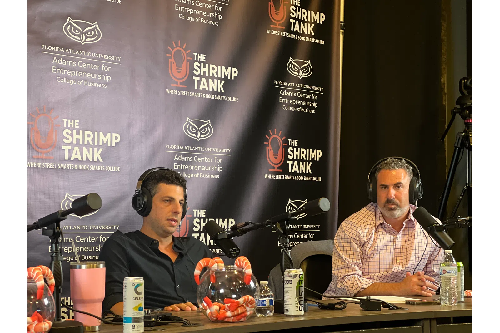 Two men wearing headphones speaking into microphones on a podcast with The Shrimp Tank banner background