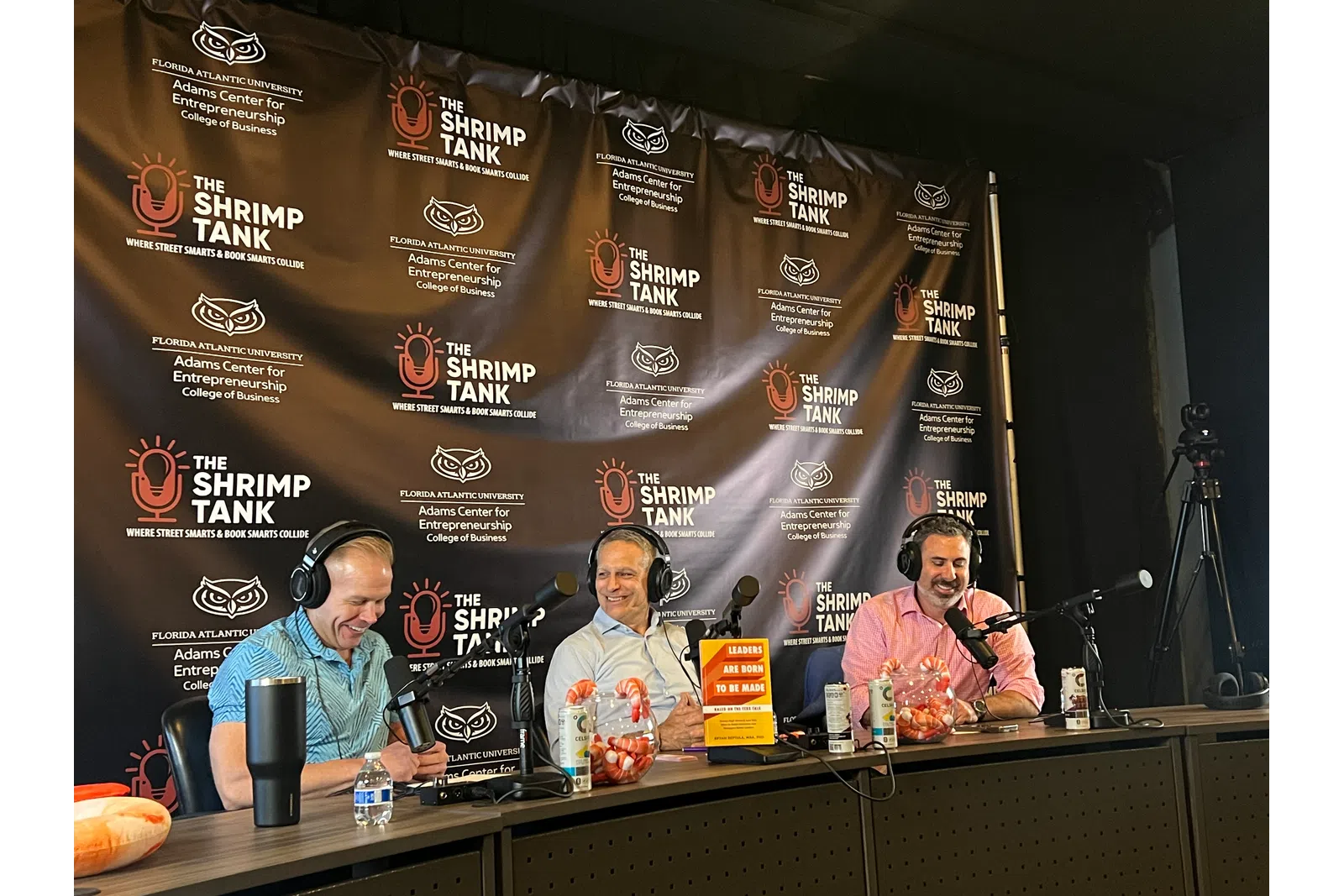 a group of people sitting at a table with microphones and a large banner behind them
