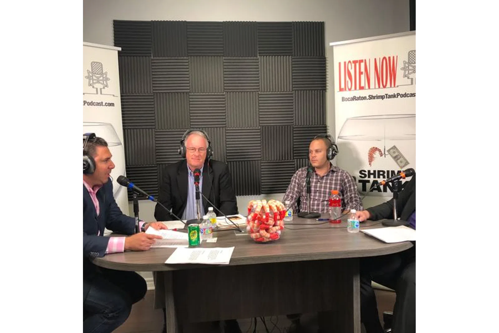 a group of men sitting at a table with microphones and a sign
