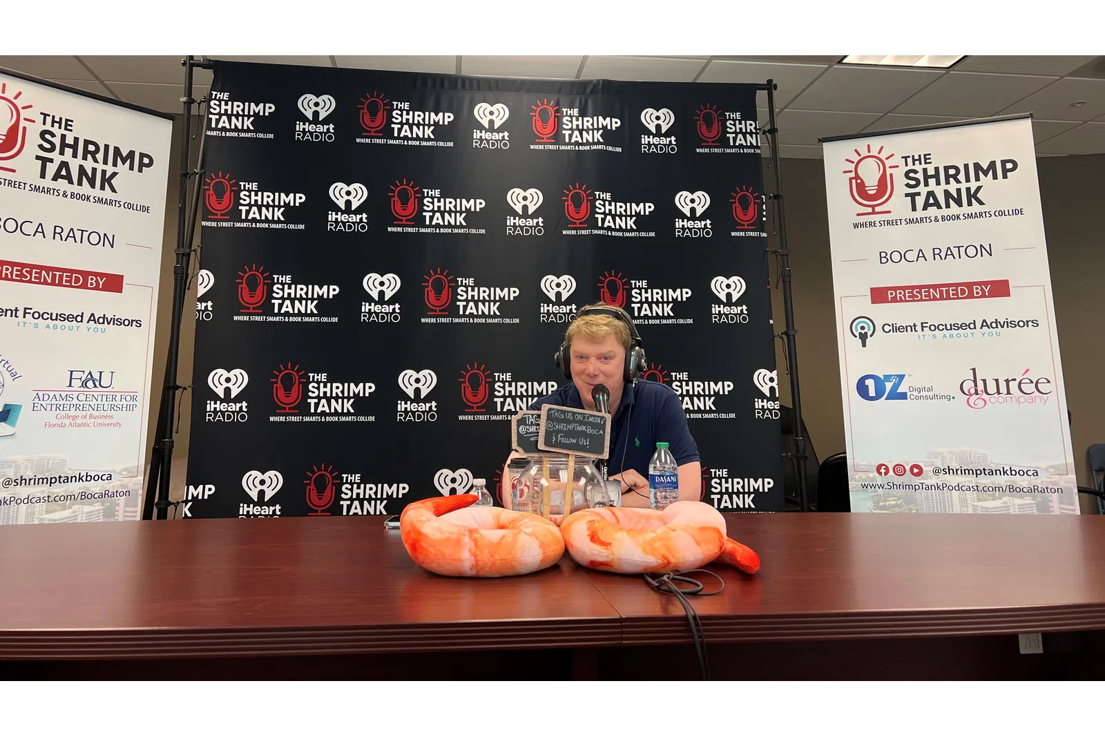 a person speaking into a microphone at a table with a couple of hot dogs