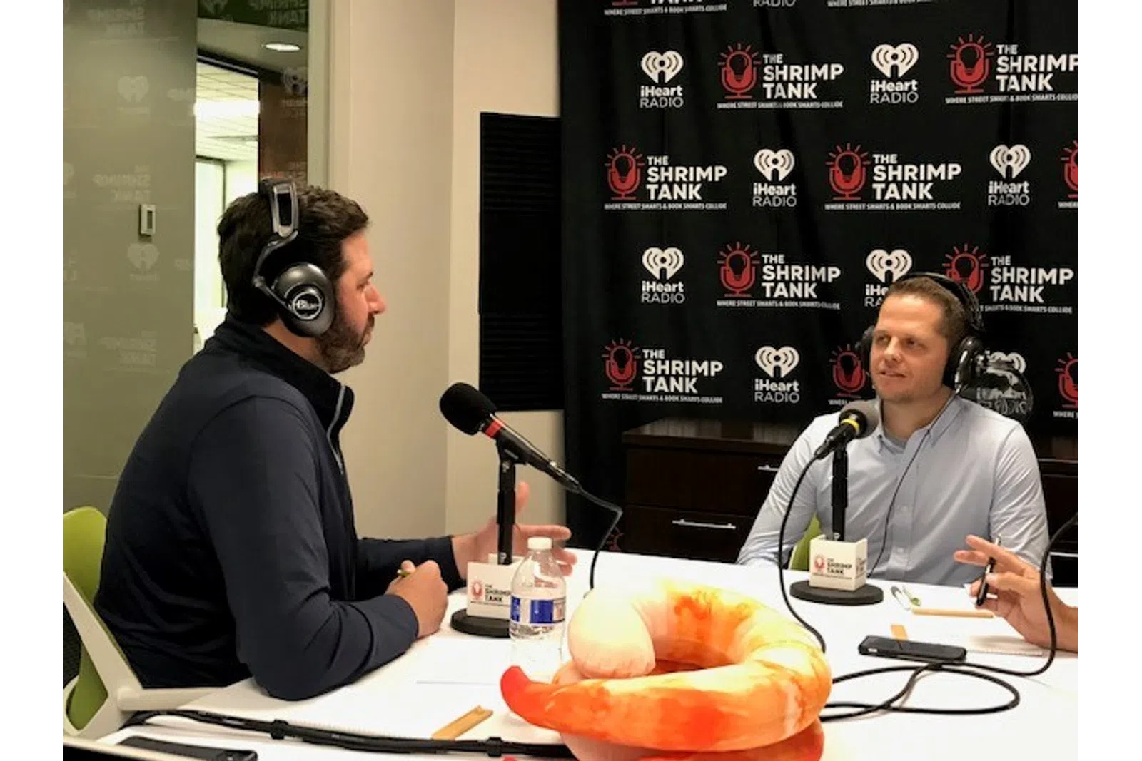Clay Steakley wearing headphones and sitting at a table with a person in a suit