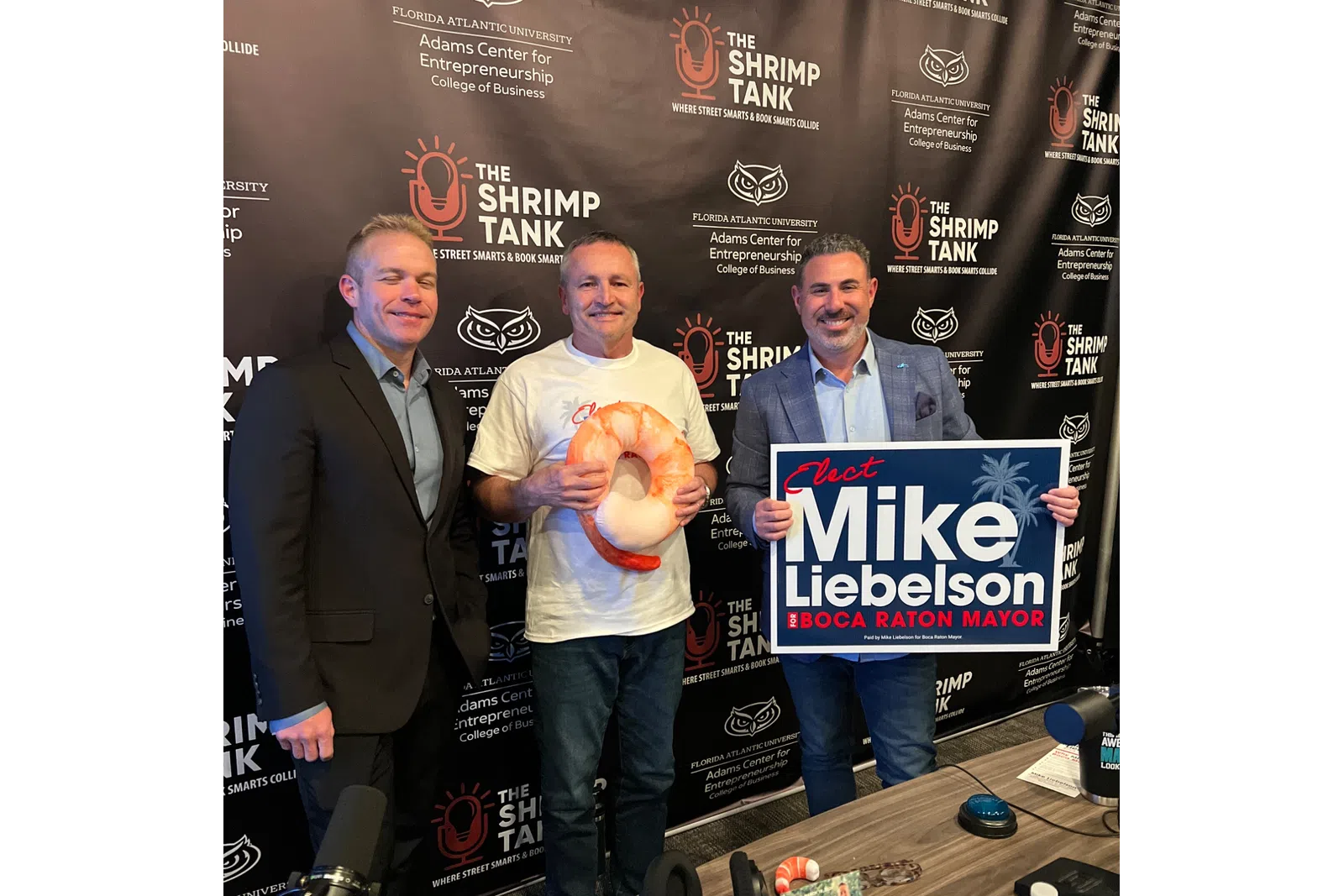 Three men at The Shrimp Tank event with campaign sign and shrimp prop, promoting Mike Liebenson for Boca Raton mayor.