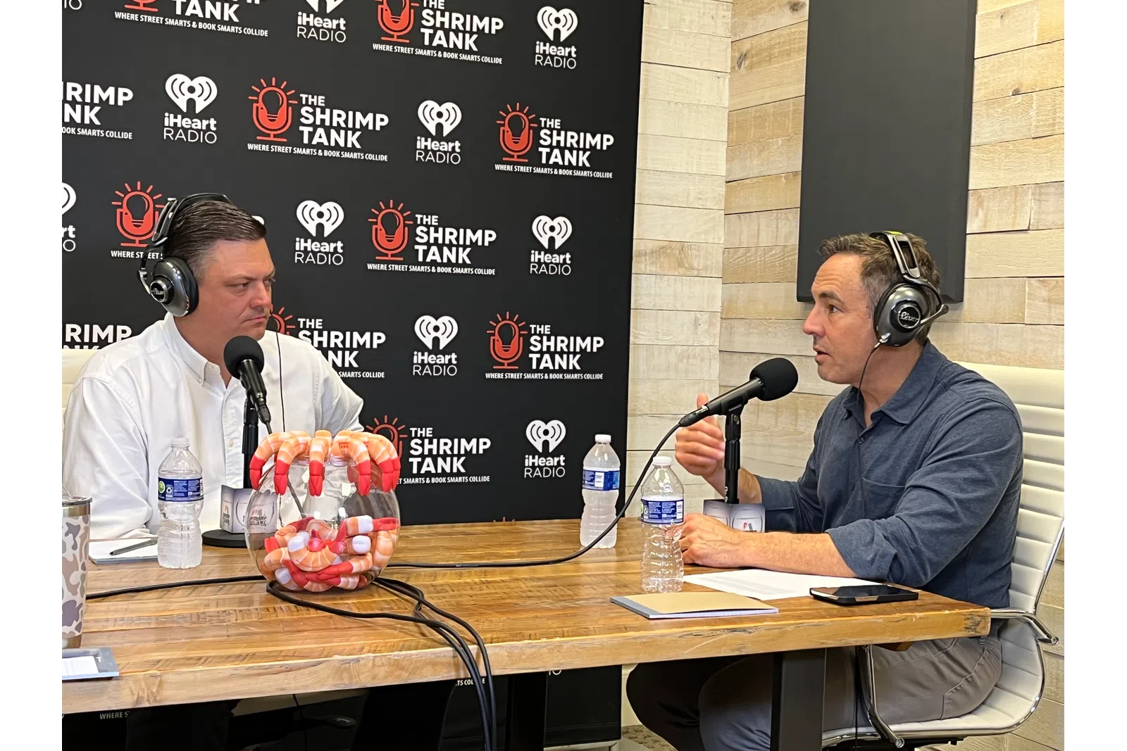 a couple of men wearing headphones and sitting at a table with microphones