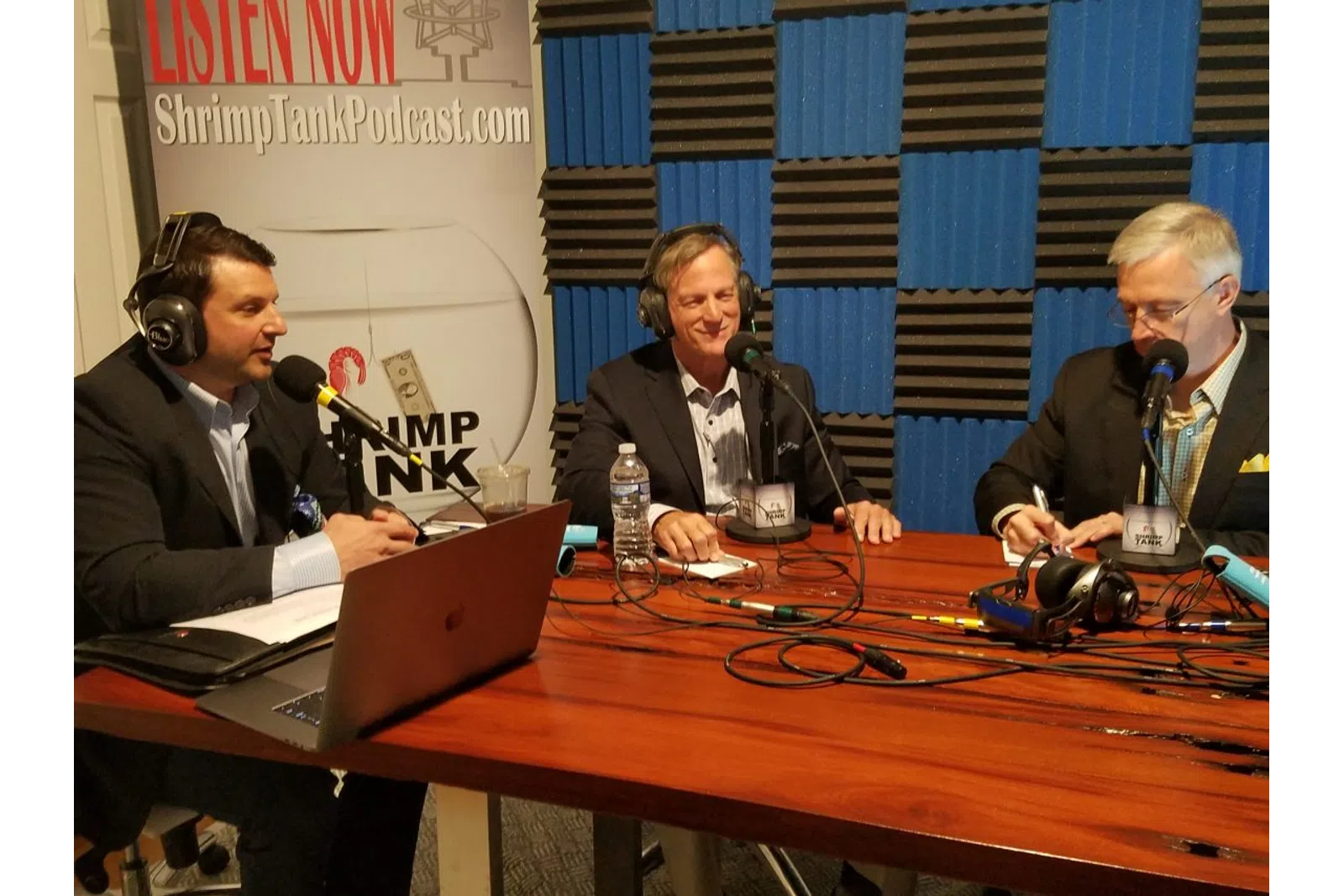 a group of men sitting at a table with microphones and a laptop