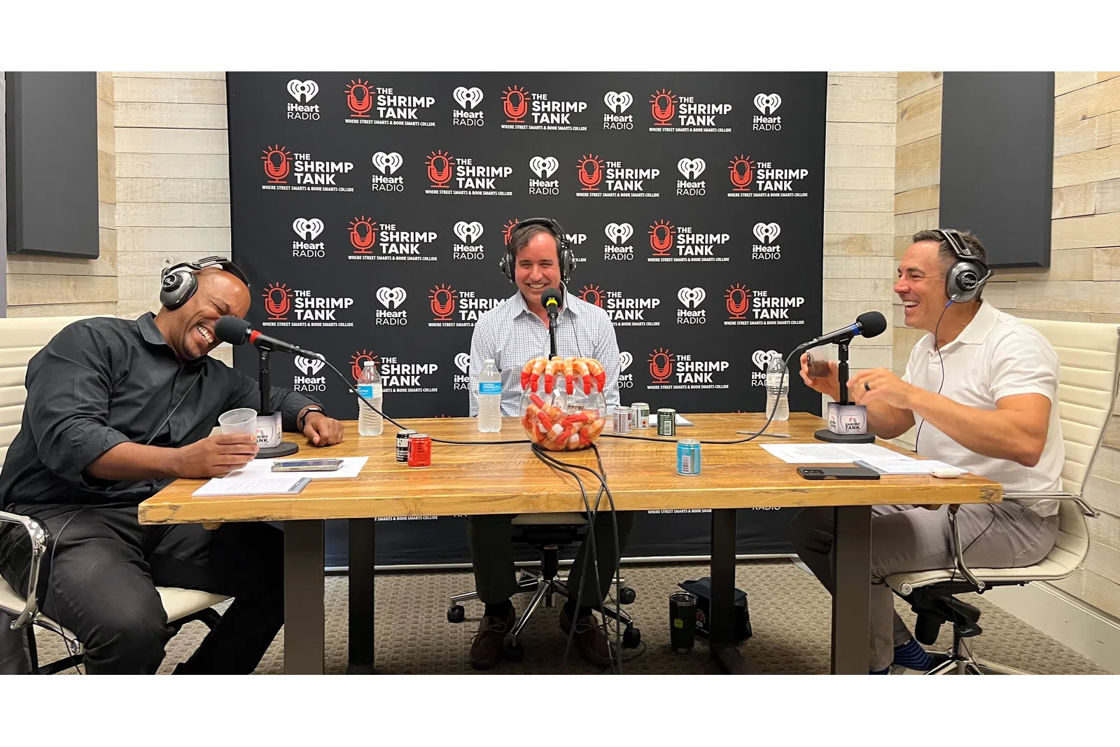 a group of men sitting at a table with microphones and a blackboard