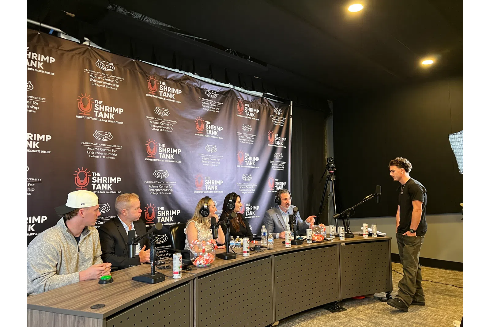Panel of five judges at The Shrimp Tank event evaluating a young presenter in a studio setting.