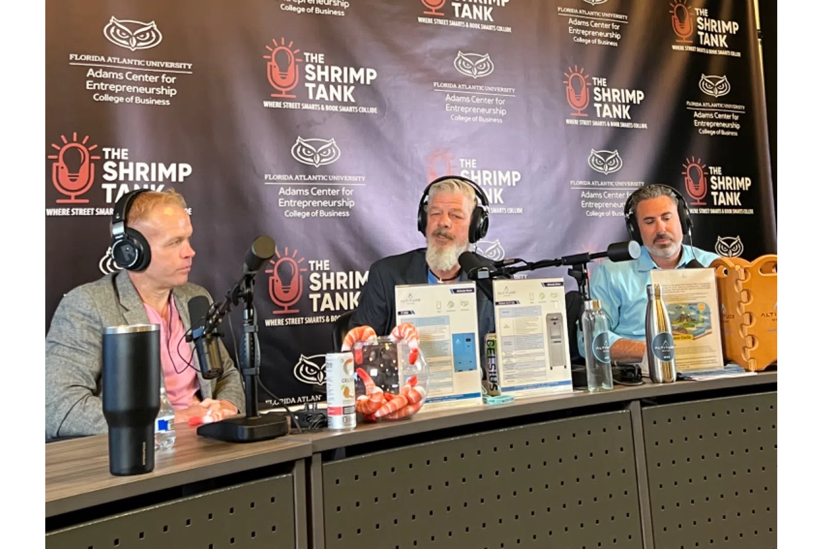 Three men discussing business ideas on a podcast set, with a branded backdrop behind them.
