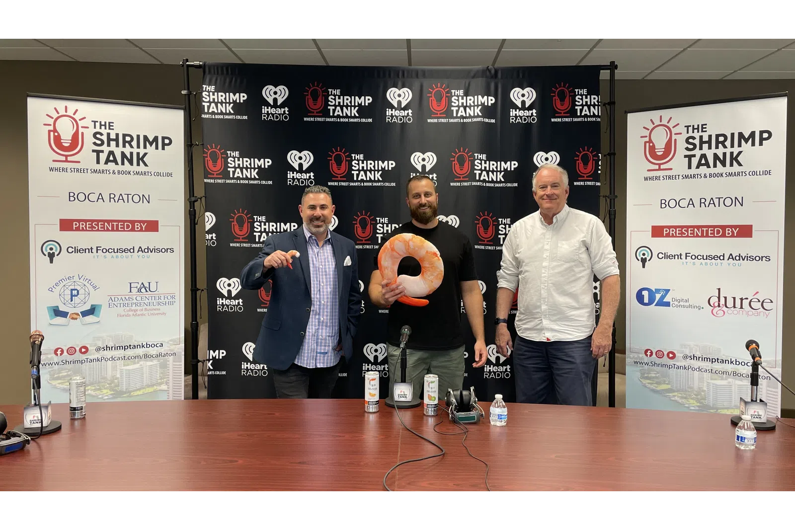 a group of men standing next to a table with microphones and a sign