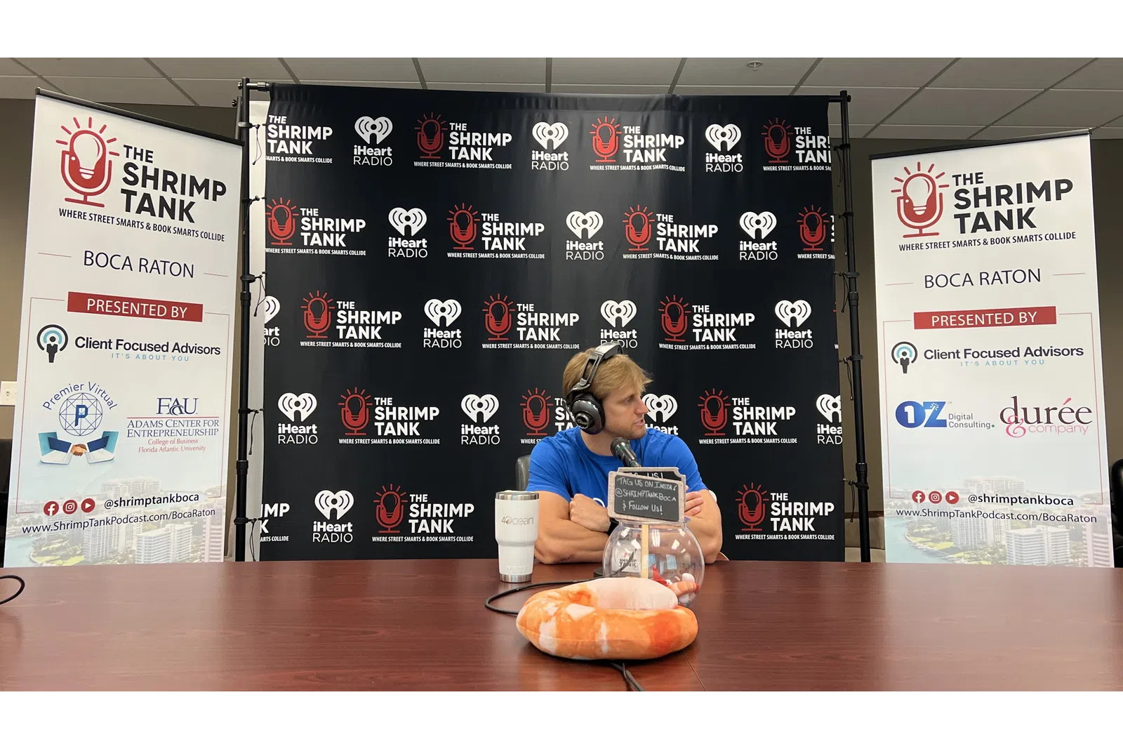 a person sitting at a table with a microphone and a sign behind the