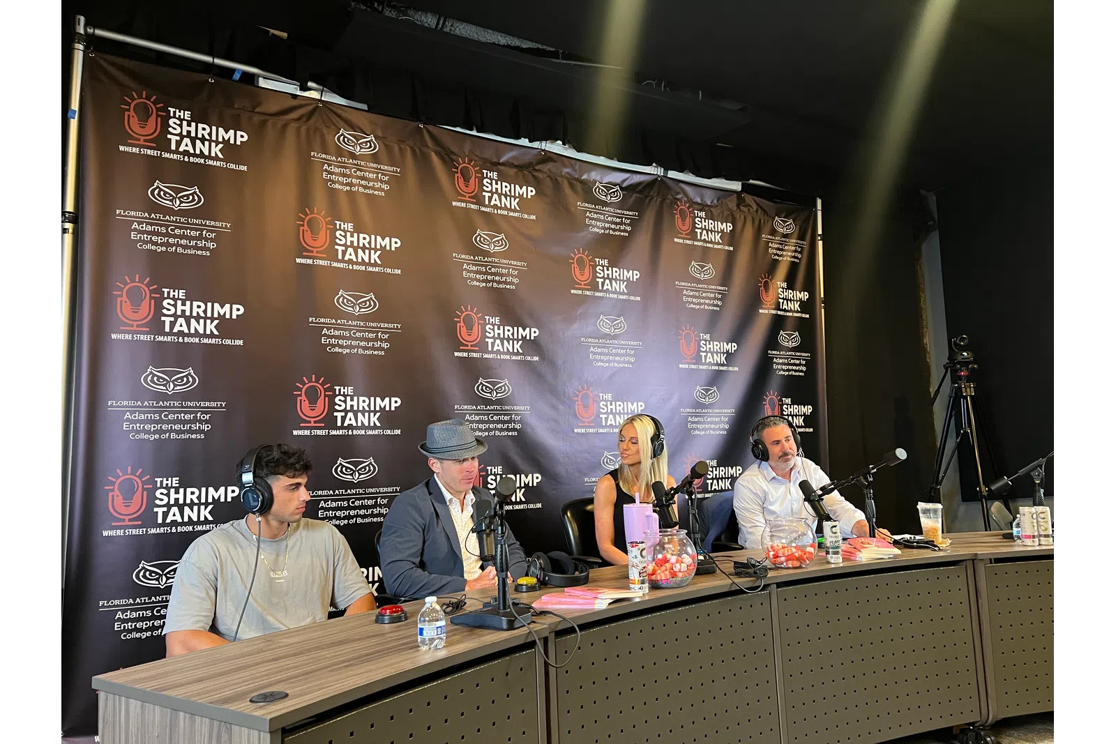 Four podcast hosts with microphones seated at a table during The Shrimp Tank by Florida Atlantic University event.