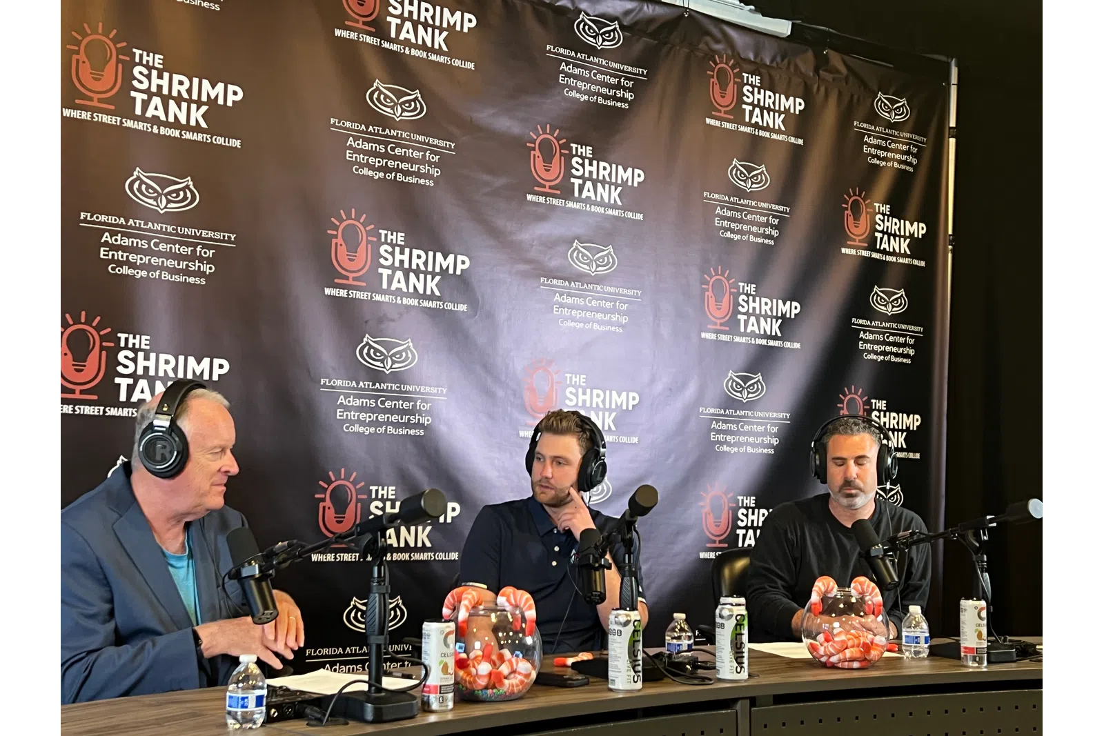 a group of men sitting at a table with microphones and a banner