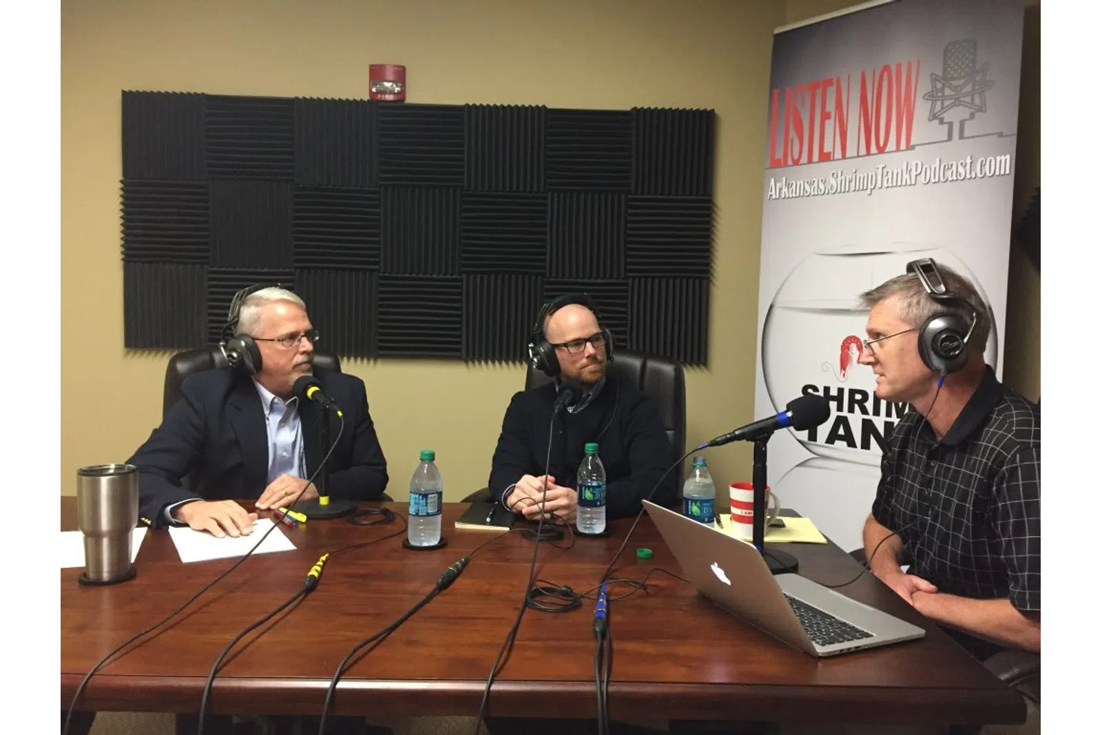 a group of men sitting at a table with microphones and laptops