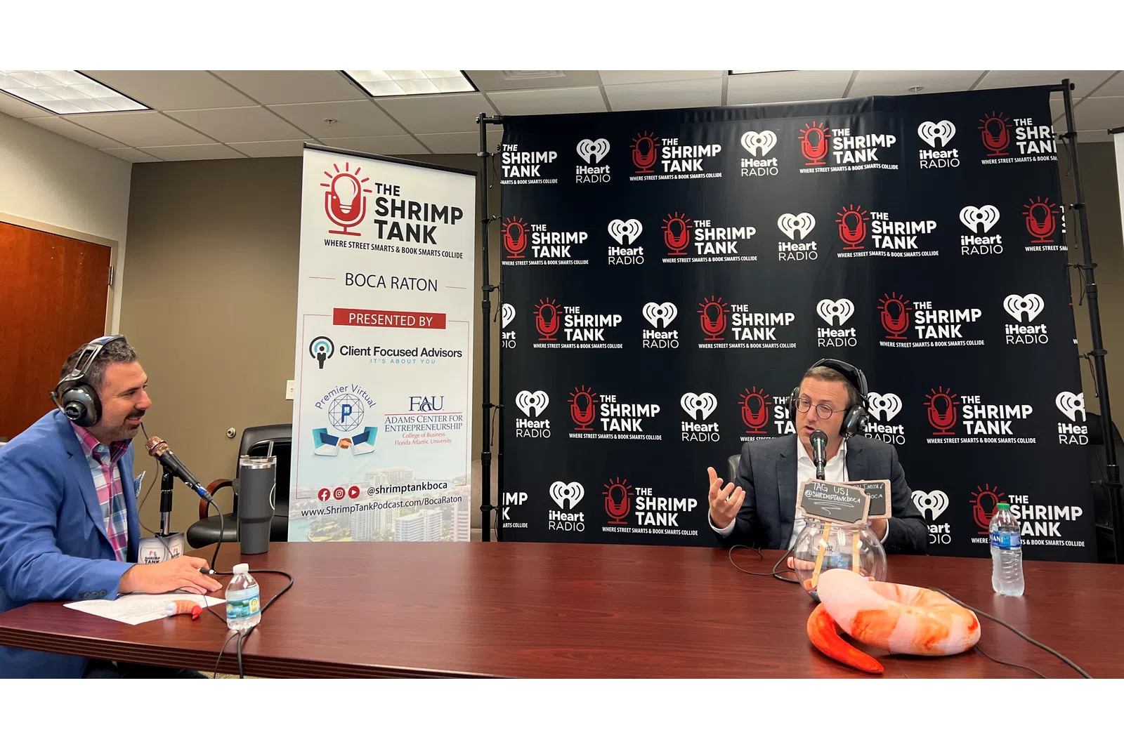 a man and woman sitting at a table with microphones and a sign