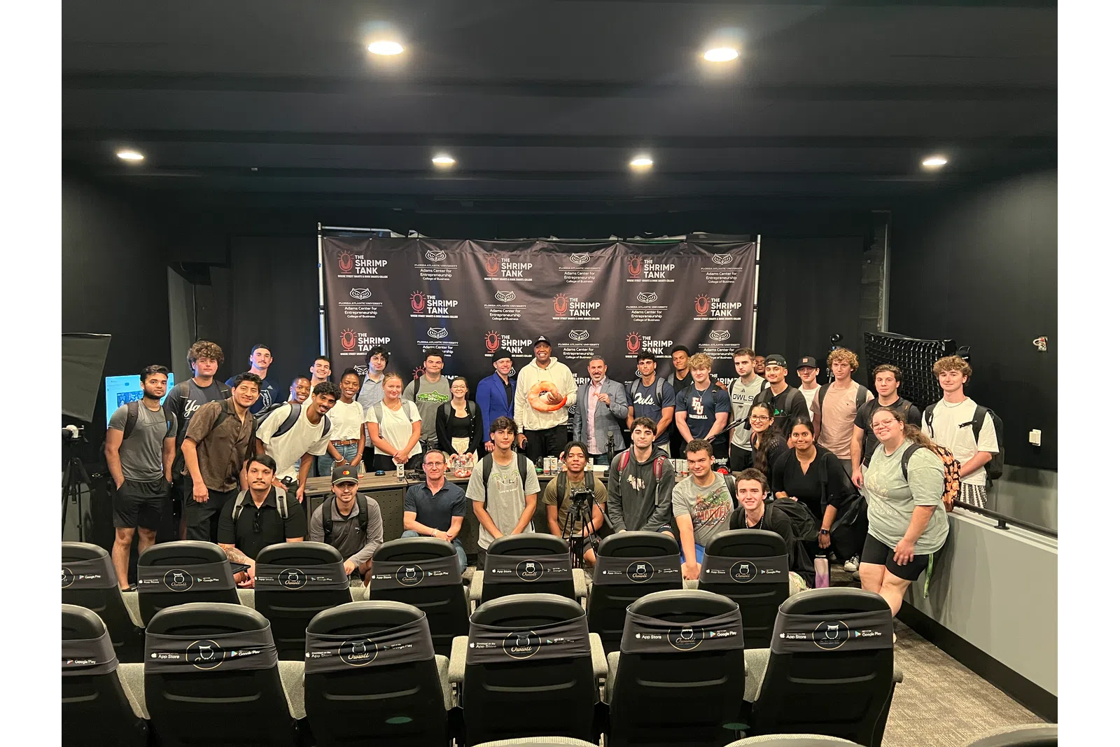 Group photo of diverse young adults in a seminar room with Shrimp Tank branding backdrop and seats in front