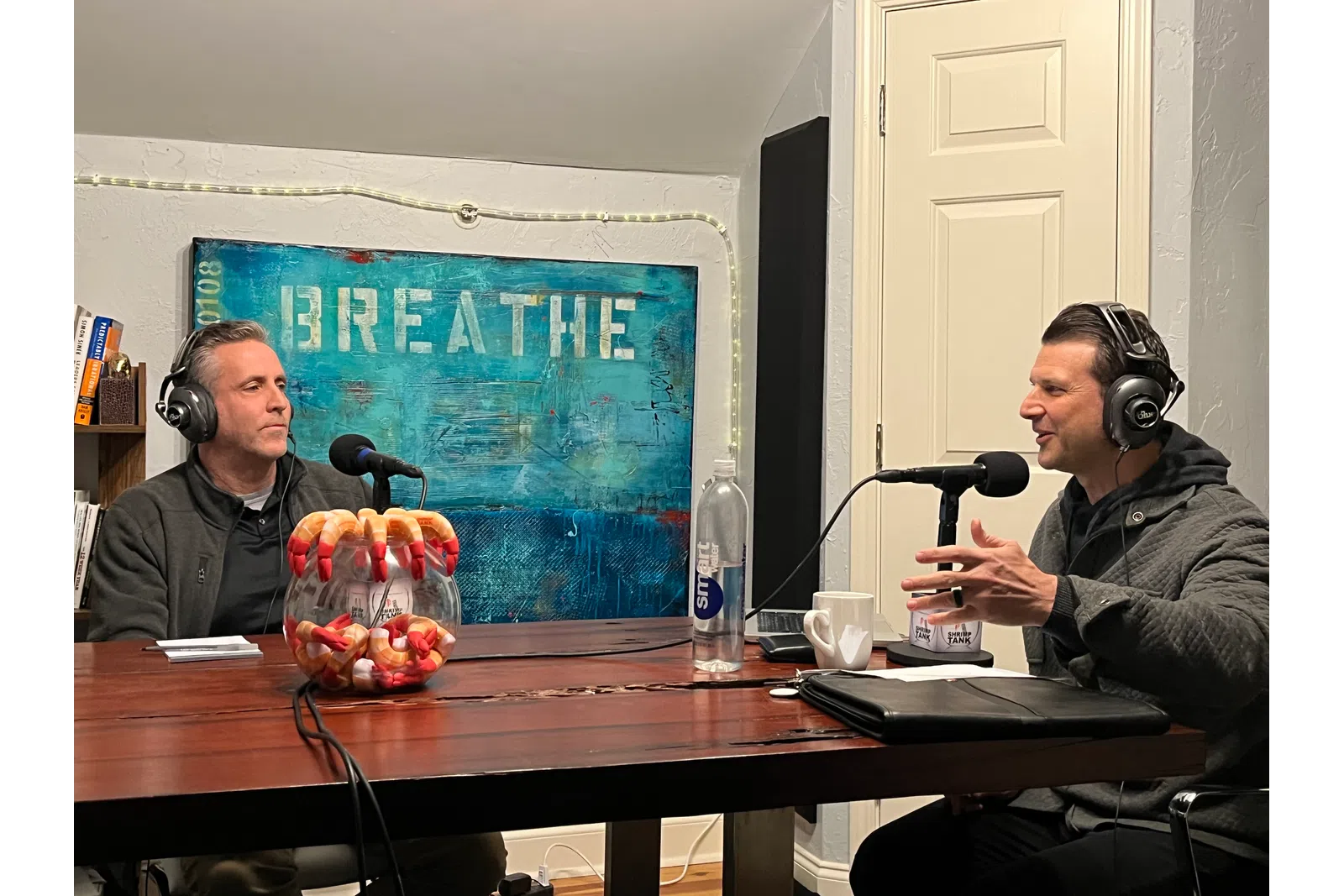 a couple of men wearing headphones and sitting at a table with microphones