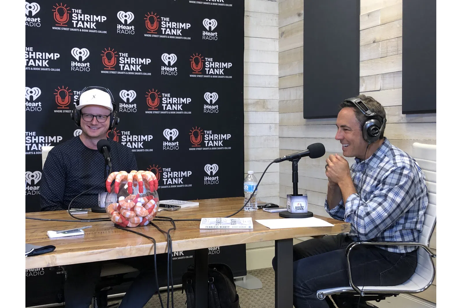 a couple of men wearing headphones and sitting at a table with microphones