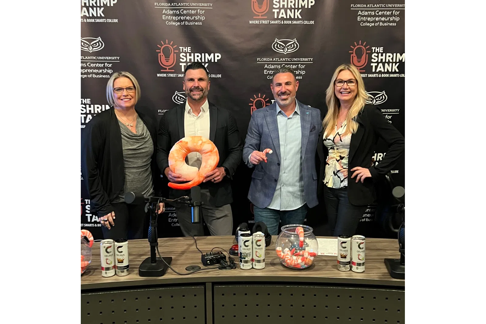 Four people smiling at a podcast table with shrimp-themed decorations and The Shrimp Tank backdrop
