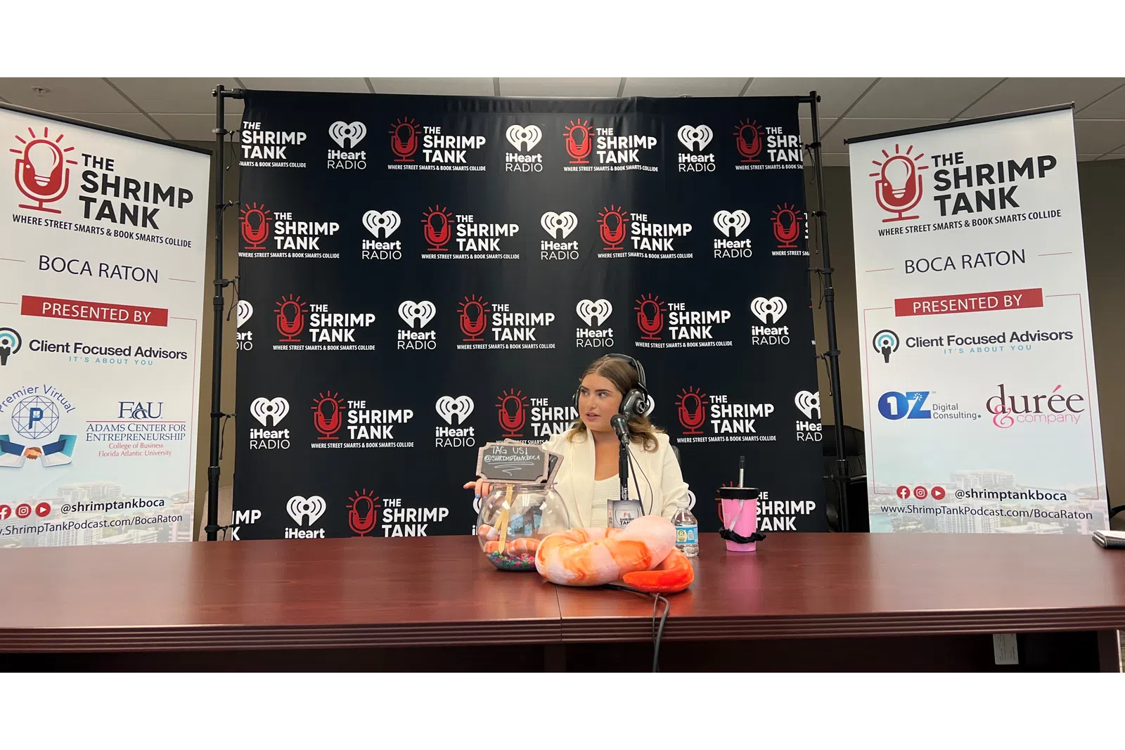 a person sitting at a desk with a microphone and a sign behind the