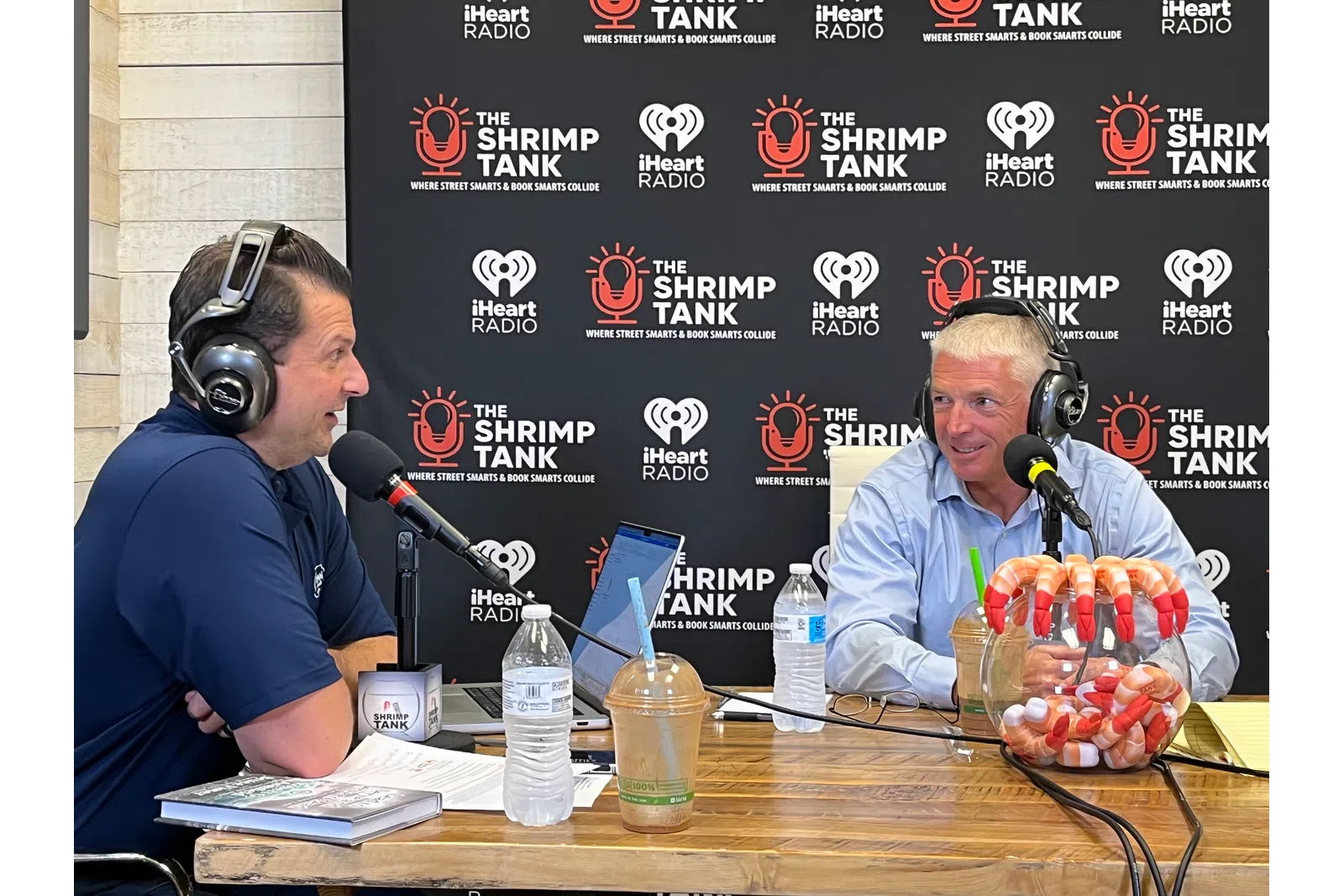 a couple of men wearing headphones and sitting at a table with microphones