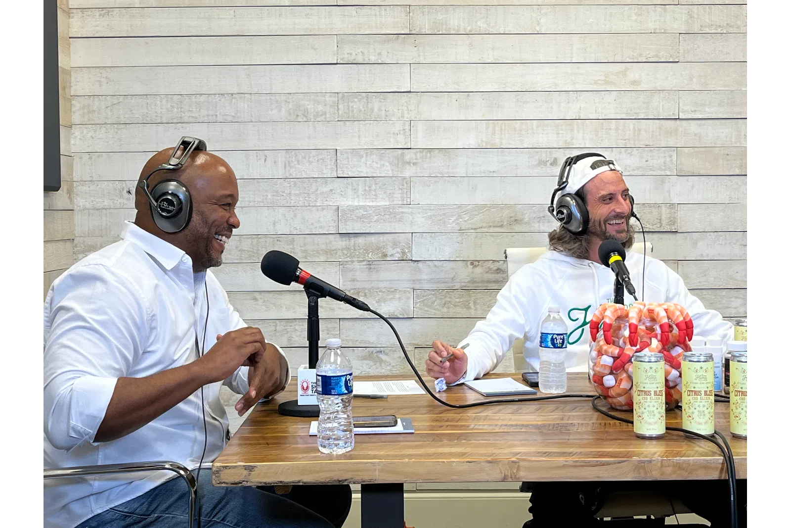 a couple of men wearing headphones and sitting at a table with microphones