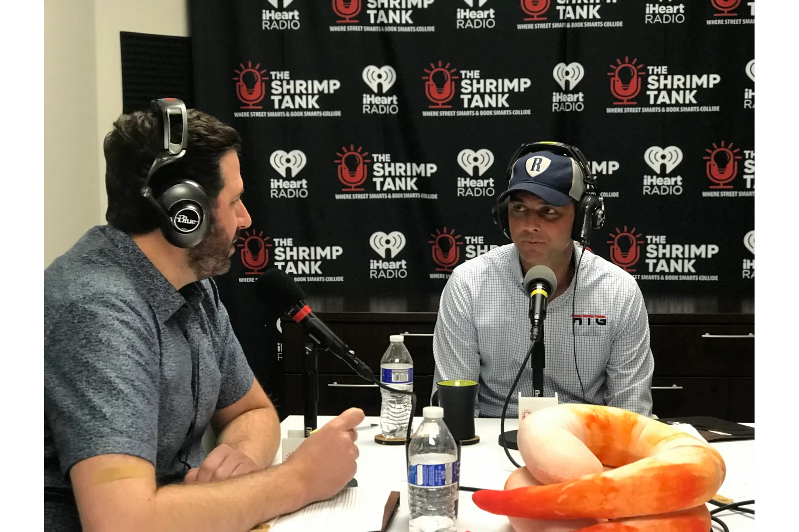 a couple of men wearing headphones and sitting at a table with a hot dog