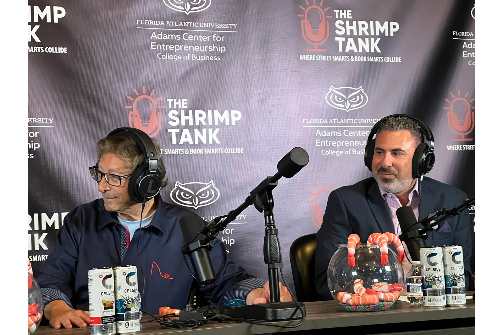 Two men with headphones sitting at a podcast table with microphones and Celsius energy drinks during The Shrimp Tank event.