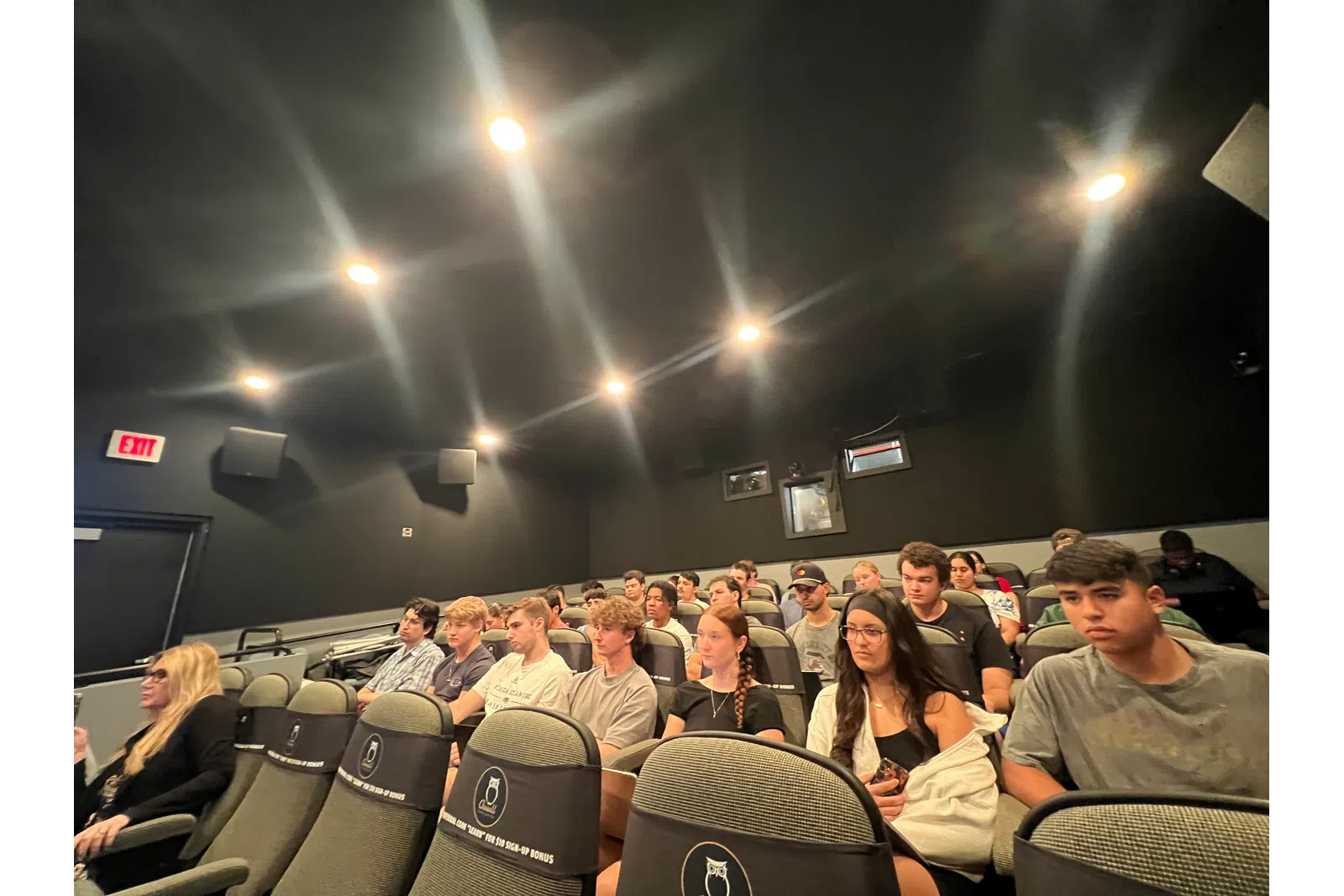 Group of young adults seated in a dark auditorium or classroom, attending an event or lecture.