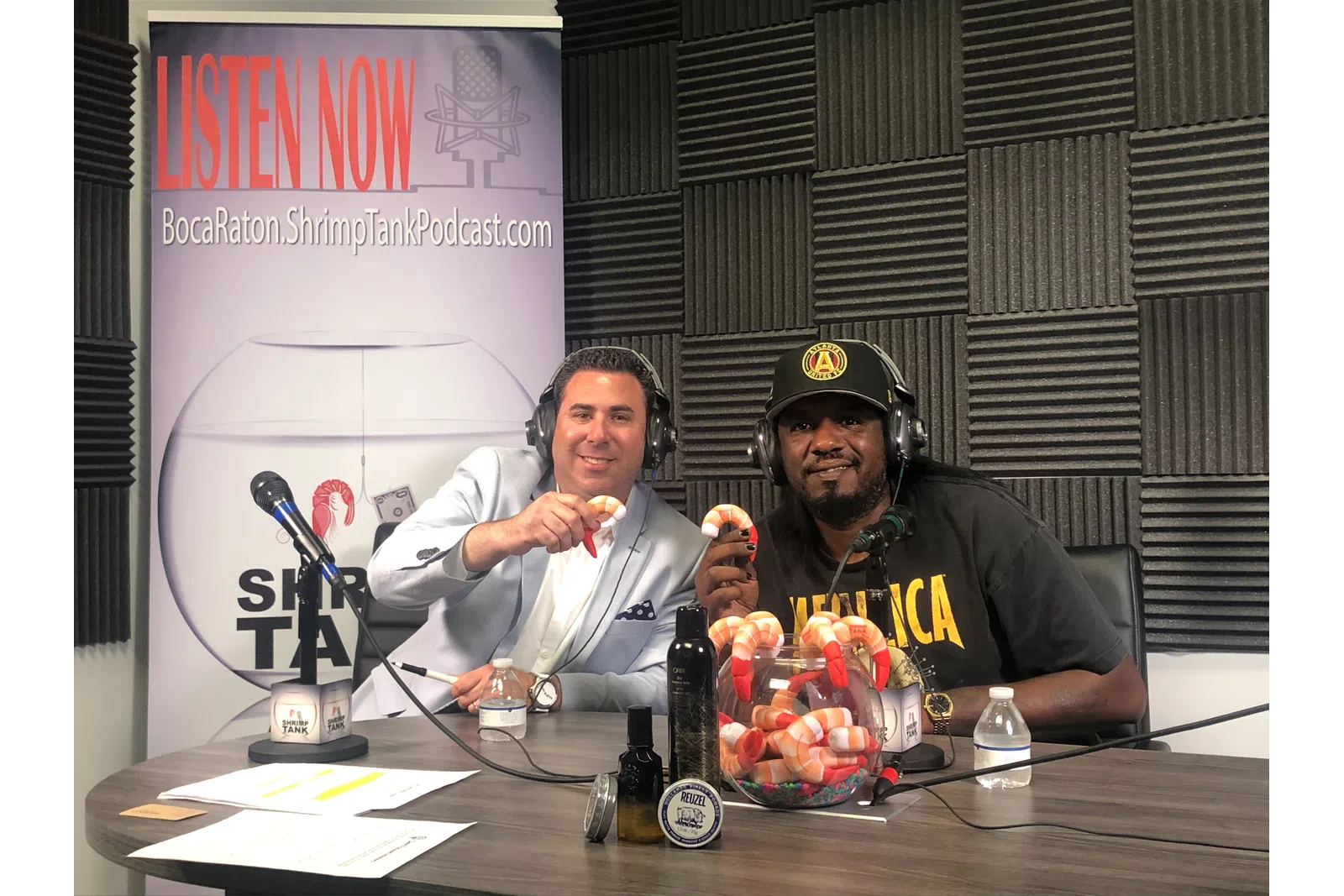 a couple of men sitting at a table with microphones and food
