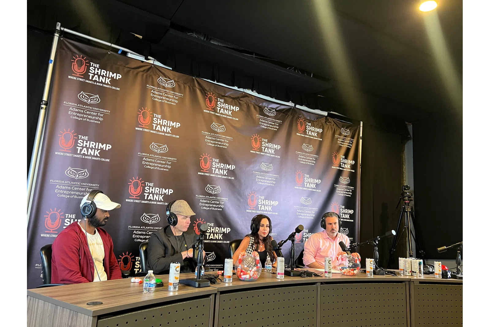 Panel of four hosts and guests with microphones at The Shrimp Tank event table with branded backdrop