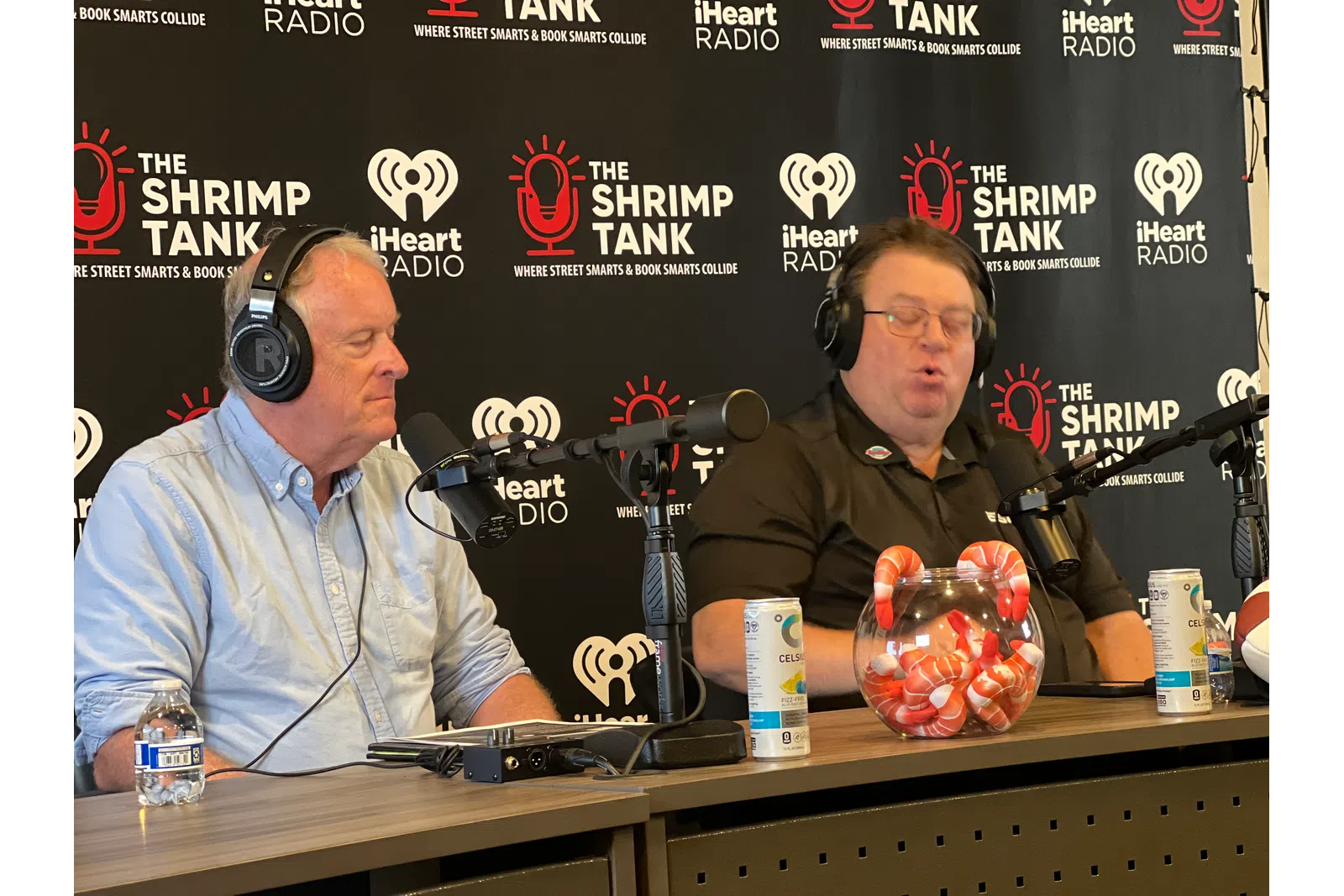 a couple of men sitting at a table with microphones and a basket of popcorn