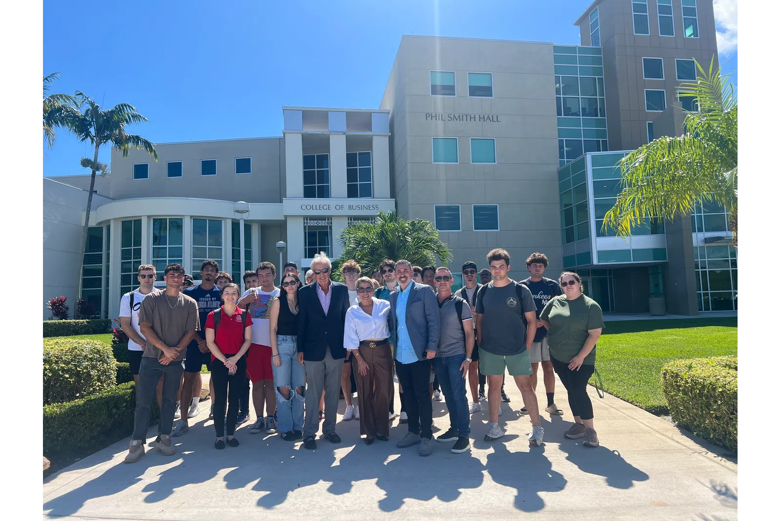 Group of students and faculty standing outside Phil Smith Hall at the College of Business on a sunny day.