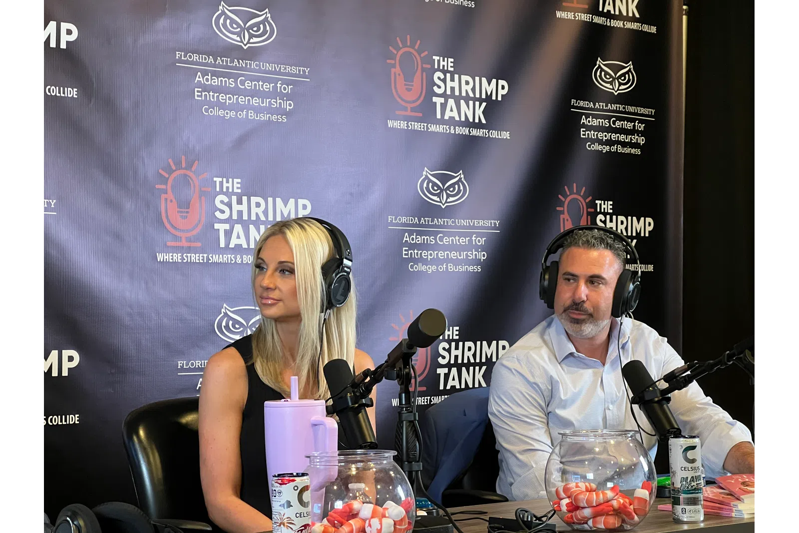 Two podcasters with headphones speaking into microphones at The Shrimp Tank podcast set with FAU branding.