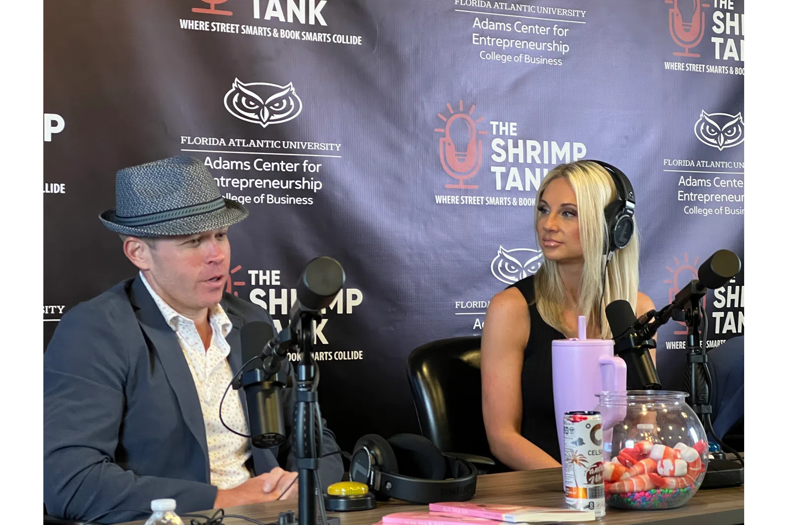 Two podcast hosts speaking into microphones during a recording at The Shrimp Tank studio.