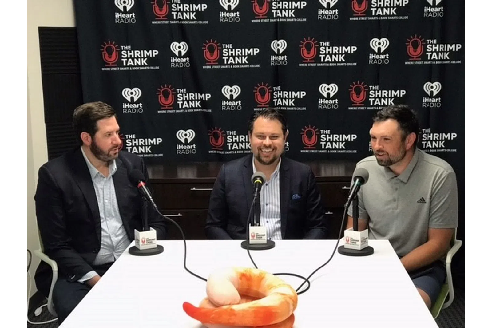 a group of men sitting at a table with microphones and a large screen behind them