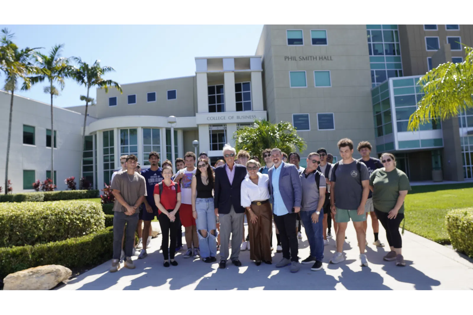 Group of diverse students and faculty posing outside Phil Smith Hall College of Business on a sunny day.