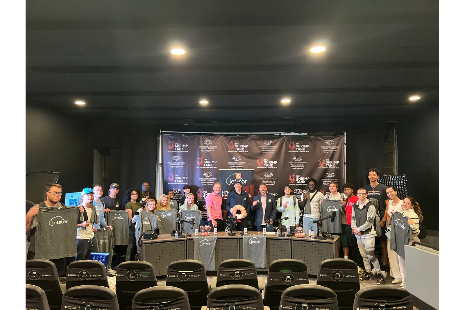 Group photo at a press event showcasing branded shirts and a logo backdrop.