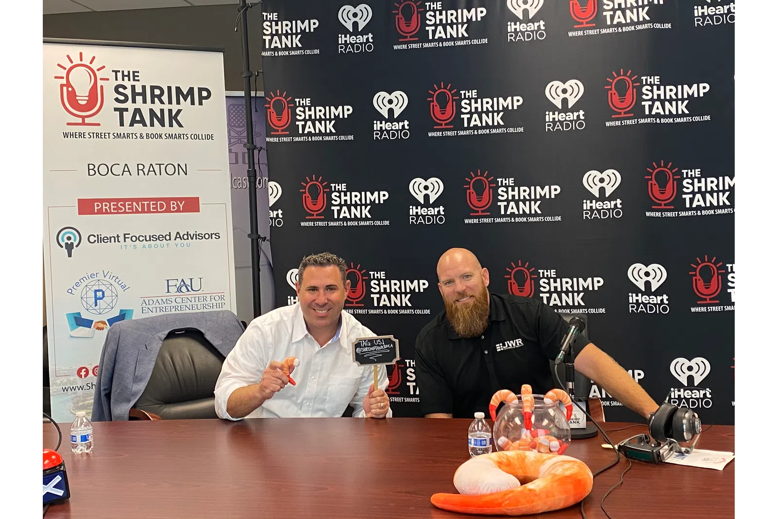 Frank Romano et al. sitting at a table with a sign behind them